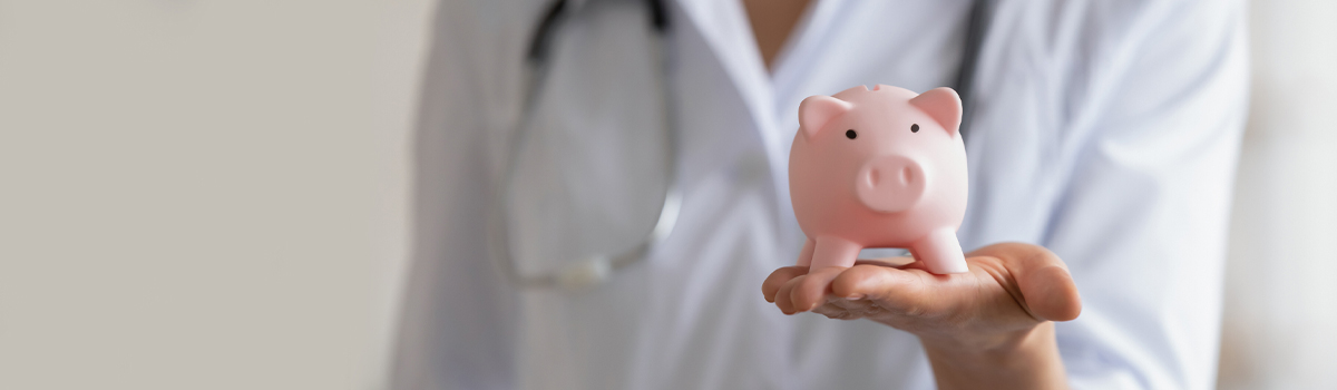 Dr in white coat wearing stethoscope has hand out holding piggy bank