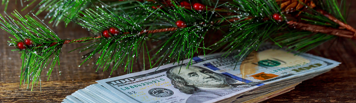 A stack of money sitting on a wooden table next to a Christmas tree.